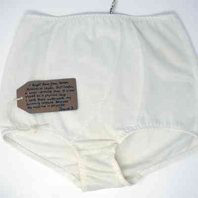 White underwear lying on a white surface. There is a brown tag with writing lay on the underwear.