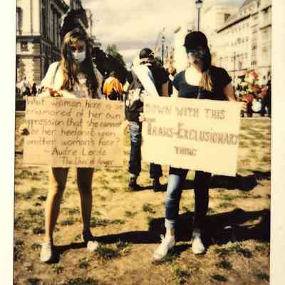 Two masked individuals hold signs at a protest in London.