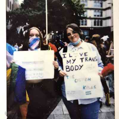 Two people at a protest hold signs advocating for transgender rights in a public gathering area.