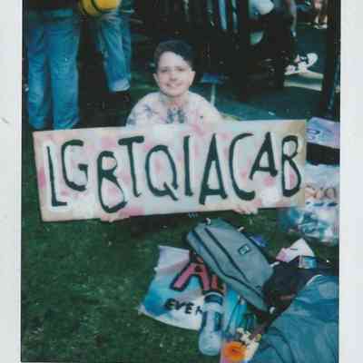 A person at London Trans Pride in Soho holds a colorful sign reading "LGBTQIACAB".