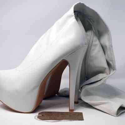 Pair of white, knee-high, high-healed boots with a brown luggage tag