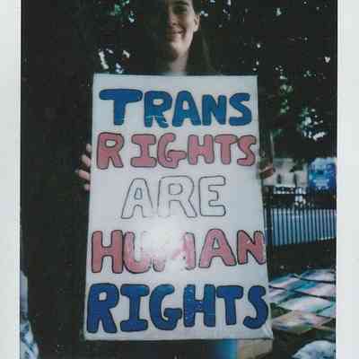 A person holds a sign reading "Trans Rights Are Human Rights" during an outdoor event.