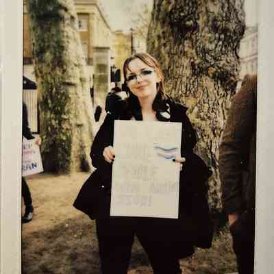 A person stands outdoors holding a sign that reads, "You can't cure people who aren't sick!"