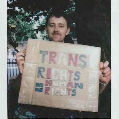 A person is holding a cardboard sign that reads "Trans rights are human rights" outdoors.