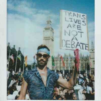 A person holds a sign saying "Trans Lives Are Not a Debate" stood in front of a crowd with Big Ben in the background.