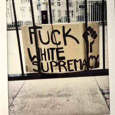 A cardboard sign saying "F*** White Supremacy" with a clenched fist, is displayed.