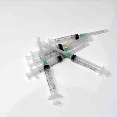 A pile of several unused syringes is scattered randomly on the plain white surface.