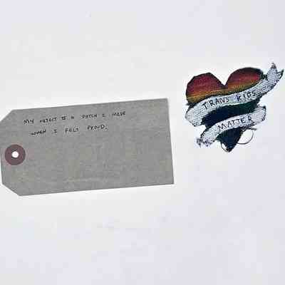 Badge patch & tag ; cotton fabric heart shaped hand painted with rainbow colours and white banner slogan " Trans Kids matter".