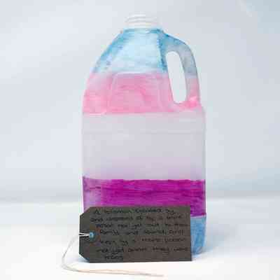 A plastic bottle hand coloured in the trans flag colours, with a brown luggage tag