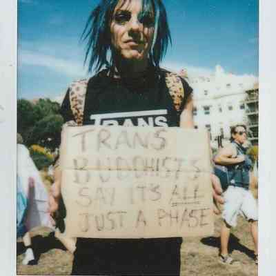 A person with blue hair holds a sign that says, "Trans Buddhists say it's all just a phase".