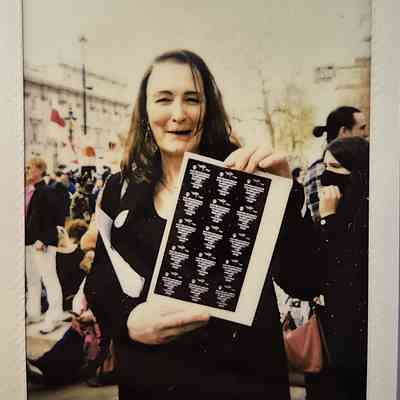 A person with long hair is smiling, holding a document in a busy outdoor setting.