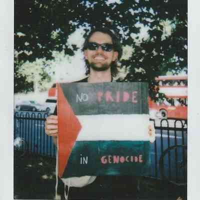 A person wearing sunglasses holds a sign reading, "No Pride in Genocide," standing outdoors.