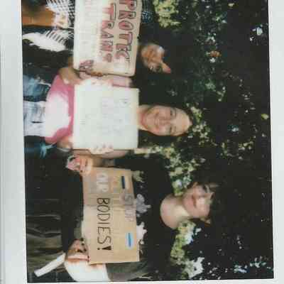 Three individuals are holding signs advocating for trans rights at an outdoor gathering in London.