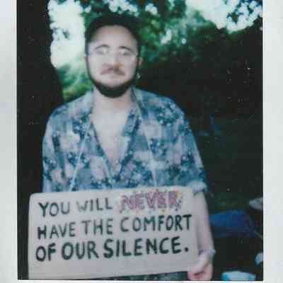A person holds a sign reading, "You will never have the comfort of our silence".