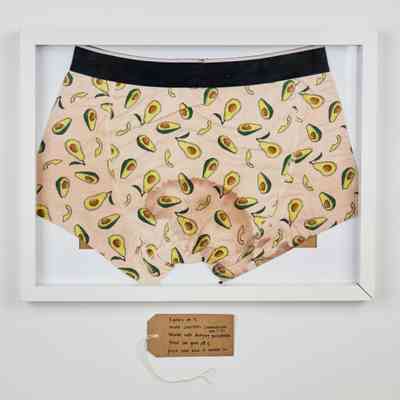A framed pair of avocado-themed underwear is displayed, featuring a handwritten tag below.