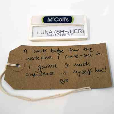 A McColl's employee name badge stating "LUNA (SHE/HER) SALES ASSISTANT" with a handwritten luggage tag.