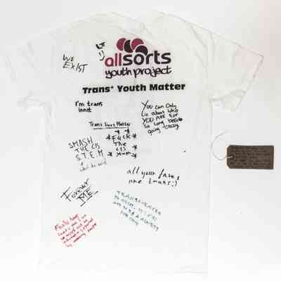 Back of the white T-shirt with the logo "allsorts youth project" at the top. Various signatures and handwritten slogans written across the back in blue, black, and red inks.