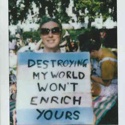 A person at London Trans Pride in Soho '22 holds a sign reading: "Destroying my world won't enrich yours".