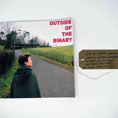 Outside of the Binary book. Cover photo is a person in a green cloak walking along a rural road. Also, a brown luggage tag.