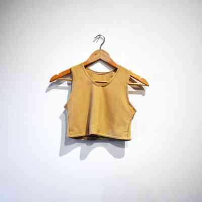 A beige cropped tank top is hanging on a wooden hanger against a plain white wall.