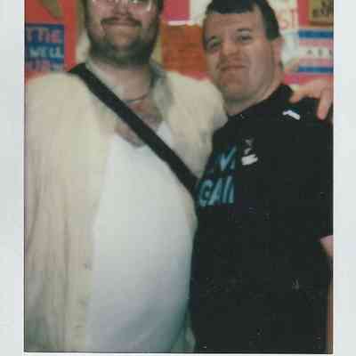 Two people smiling stand together in front of colorful posters.