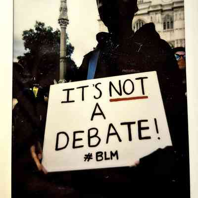 A person holds a sign reading "IT'S NOT A DEBATE! #BLM" at a protest.