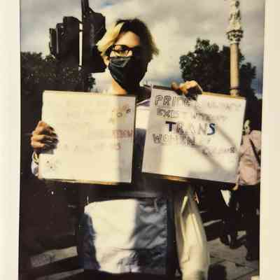 A person in a mask holds two protest signs supporting trans rights at a London event.