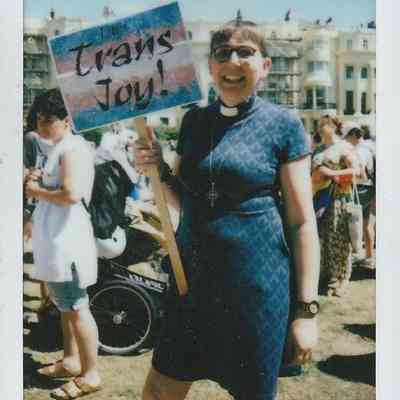 A person is smiling, holding a "Trans Joy!" sign.