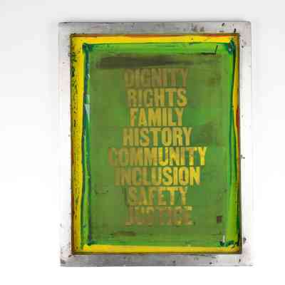 The image features a rectangular screen with 'DIGNITY RIGHTS FAMILY HISTORY COMMUNITY INCLUSION SAFETY JUSTICE'. The screen is generally green with a border of yellow and the text is yellow.
