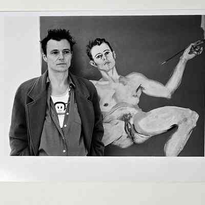 A black and white photograph of a person stood in front of a painting.