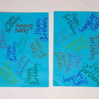 The image shows two blue sheets with "Happy Birthday" written repeatedly in various colors.