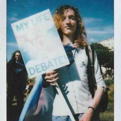 A person stands outdoors holding a sign reading "My life is not a debate".