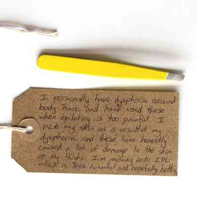The image shows a cardboard tag with handwritten text and a pair of yellow tweezers on white background.