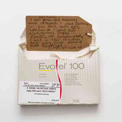 Light grey "Evorel 100" box which has been opened at the top. There is a white prescription label in the bottom left corner of the front of the box.