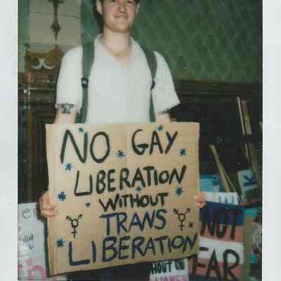 A person holds a sign saying “No gay liberation without trans liberation” at an event.
