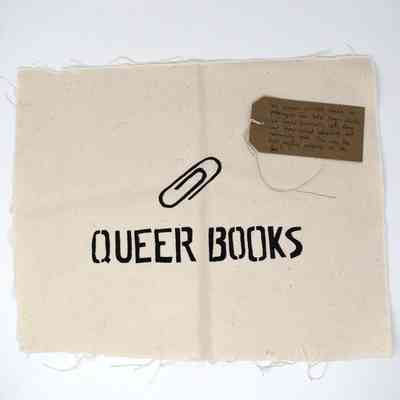 A square piece of fabric displays the words "Queer Books" with a paperclip icon above.