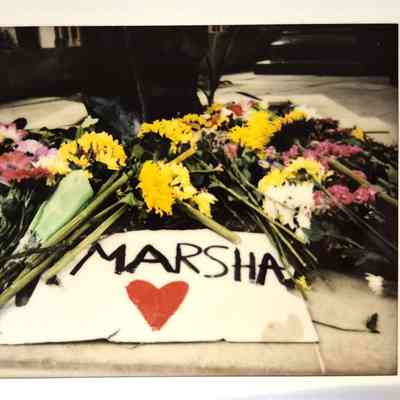 A collection of colorful flowers surrounds a sign reading "MARSHA" with a red heart.