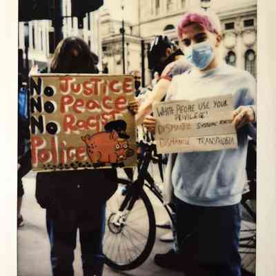 Two people hold protest signs at a protest.