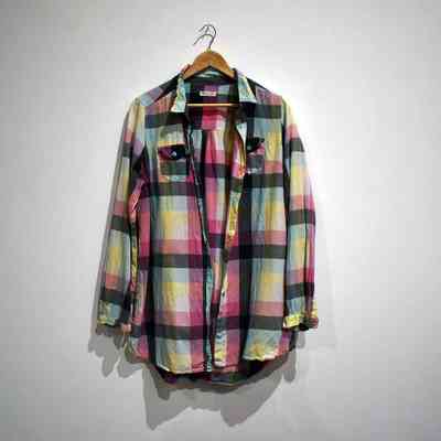 A colorful plaid shirt is displayed on a wooden hanger against a plain white wall.