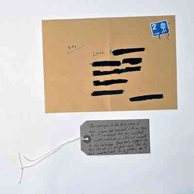 The image shows an envelope with details redacted in black and a handwritten note attached below.