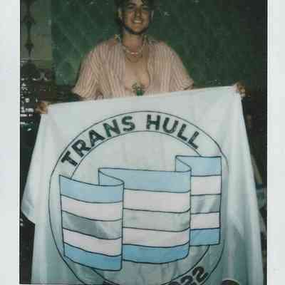 A person smiles while holding a banner that reads "Trans Hull," with handwritten text below.