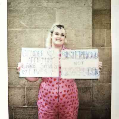 A person in heart-patterned clothing holds two placards.