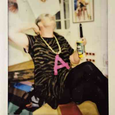 A person is sitting casually, wearing a leopard print top, large necklace with "A".