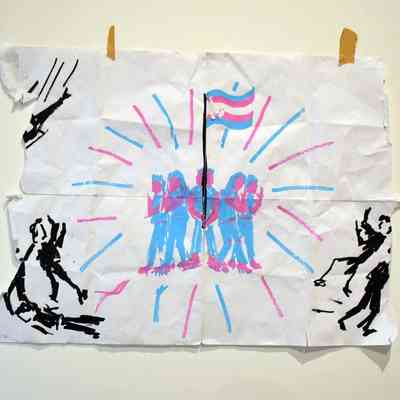 The image shows a ripped and folded piece of paper featuring five abstract figures in blue and pink around a trans pride flag, with blue and pink lines coming from them. There are figures in black around them and a helicopter to the top left..