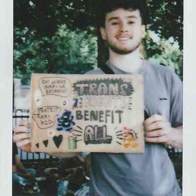 A person is holding a handmade sign advocating for transgender rights at an outdoor event in London.