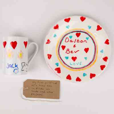 A home made mug and plate made in prison in white ceramic decorated with red and blue hearts. The plate has the text "Dalton & Bev Love". The  mug has the text "Jack" and "Dalton". With a brown, handwritten luggage tag.