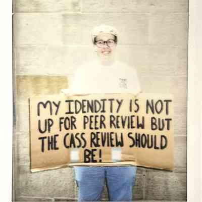 A person holds a cardboard sign with a message about identity smiling in front of a stone