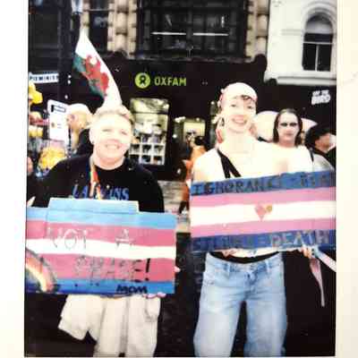 Two people stand together holding colorful protest signs in a lively urban street setting.