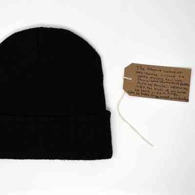 A black beanie is placed beside a handwritten tag with attached string.