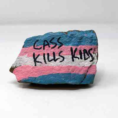 A painted stone displays the words "CASS KILLS KIDS" with colorful stripes.